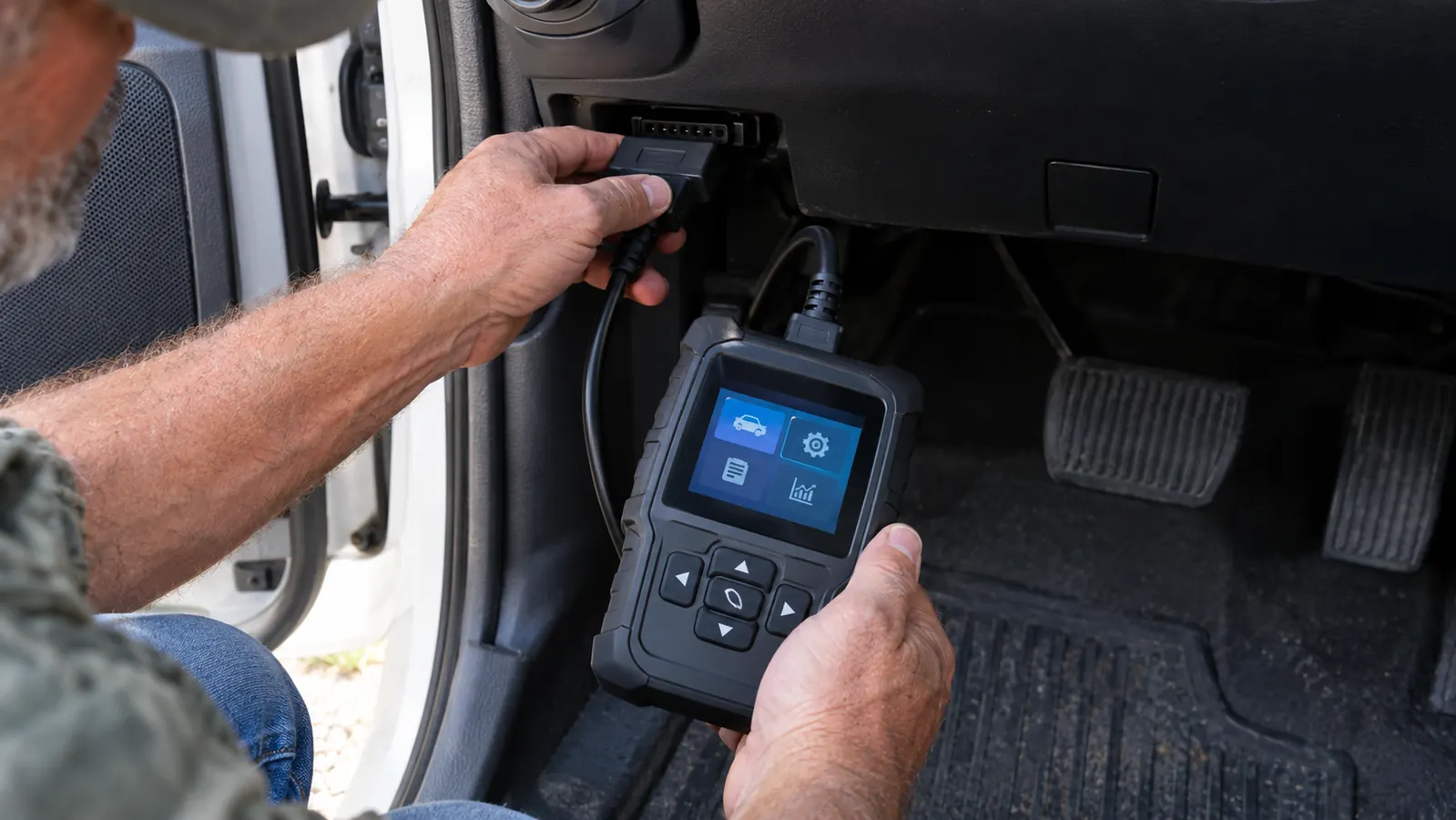 Hand plugging a code scanner into the diagnostic port under a truck's dashboard