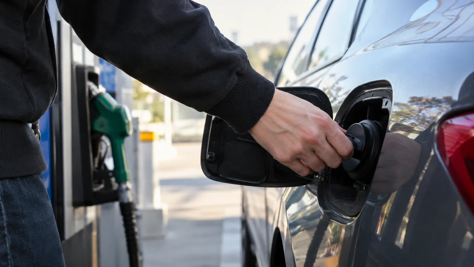 A hand tightening the gas cap on a car at a fuel station in the morning
