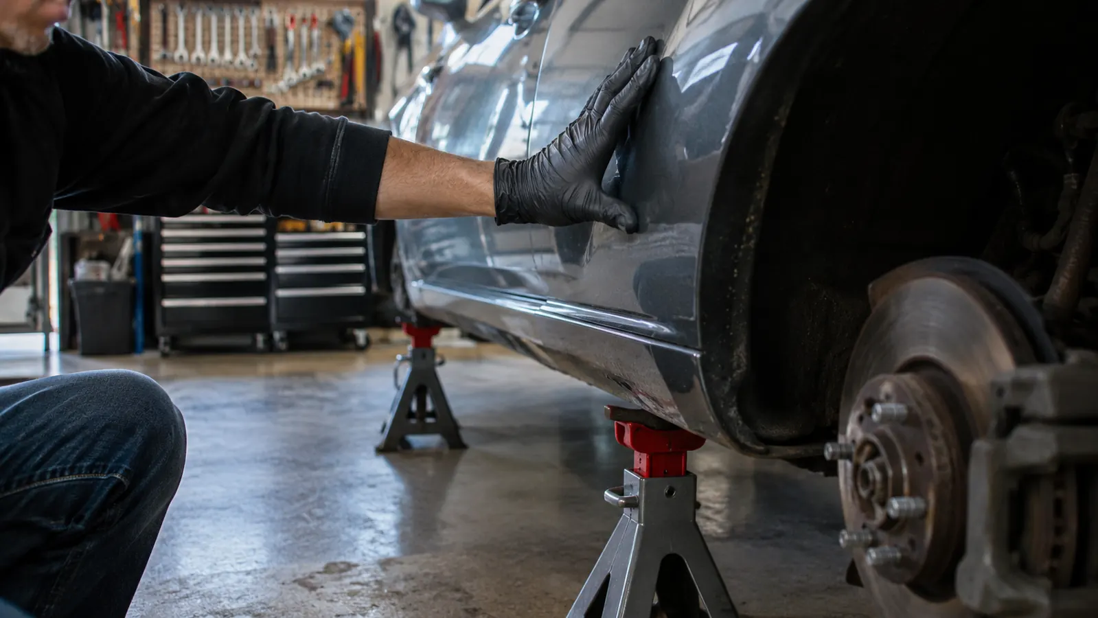 A gloved hand pushing on a car fender to test that it is steady on its jack stands